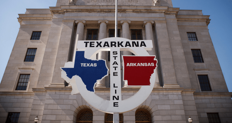 Texarkana State Line sign showing Texas and Arkansas split with government building centered behind the sign
