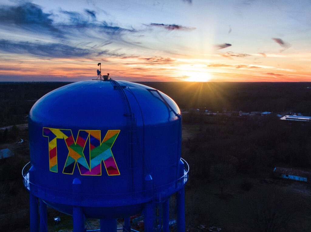 Vibrant blue water tower at sunset with rainbow painted letters TXK